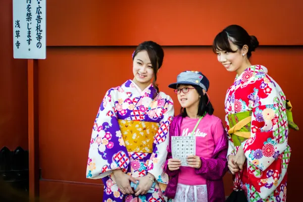 Three visitors in colourful clothing posing against an orange wall