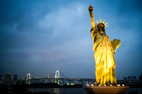 A golden Statue of Liberty replica overlooking a bridge at dusk