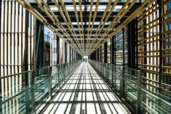 Repeating wooden beams casting geometric shadows along a glass walkway