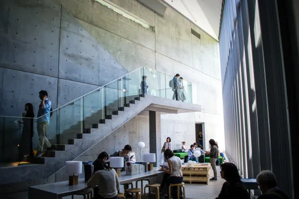 Visitors beneath a concrete staircase in a tall sunlit interior