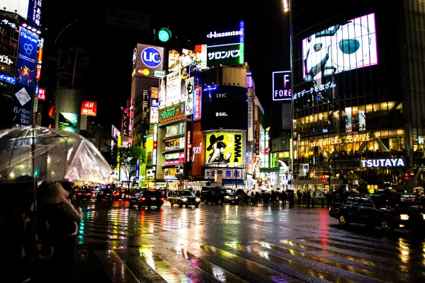 Bright city signs reflected across a rain-soaked crossing at night