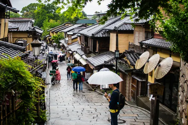 Umbrellas descending a rain-soaked street between traditional wooden houses