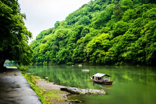 A small covered boat on a green river beneath a wooded hillside