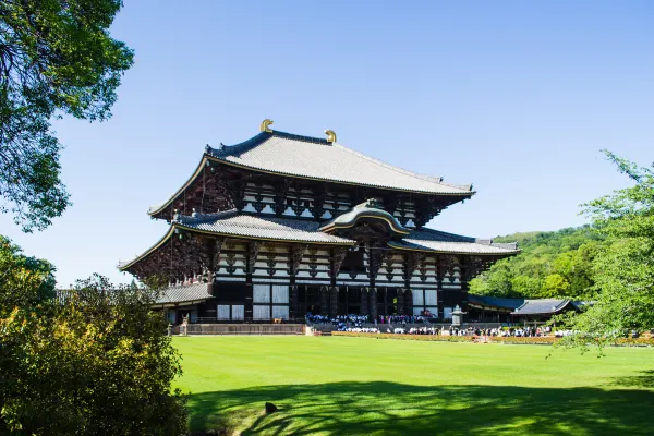 A large wooden temple beyond an open green lawn