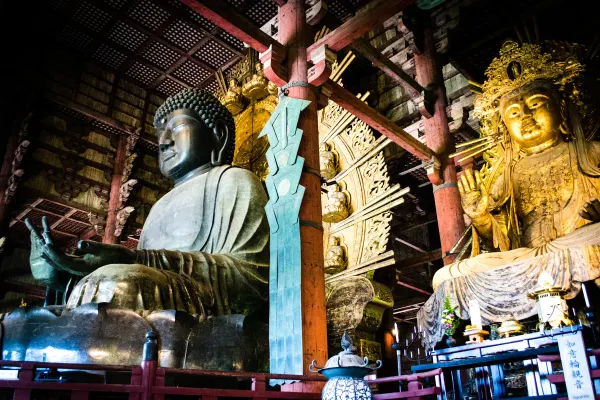 A monumental seated Buddha beneath dark timber beams and golden figures