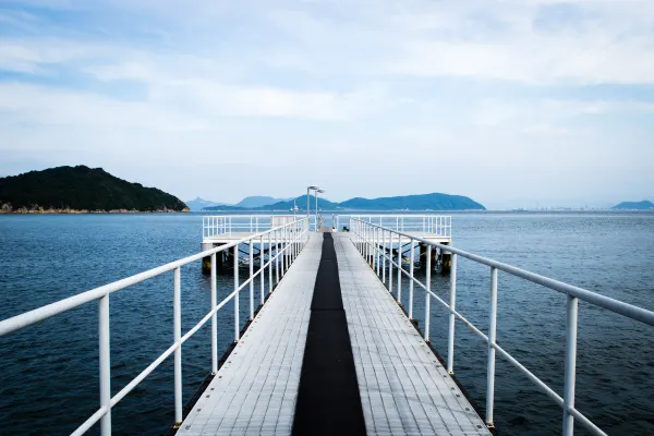 A narrow white-railed pier extending towards distant islands