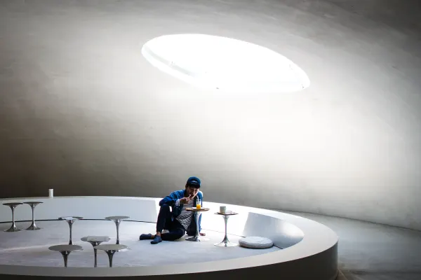 A person sitting beneath an oval skylight in a curved white interior