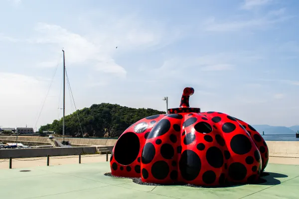 A red polka-dot pumpkin sculpture beside a quiet harbour