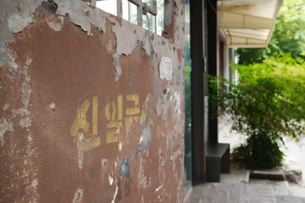 Faded yellow lettering on a weathered wall beside a leafy doorway