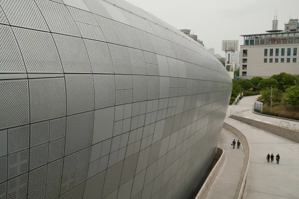 People walking beside a sweeping curved facade of perforated metal panels