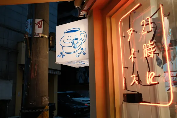 Warm orange neon lettering beside an illustrated shop sign at dusk
