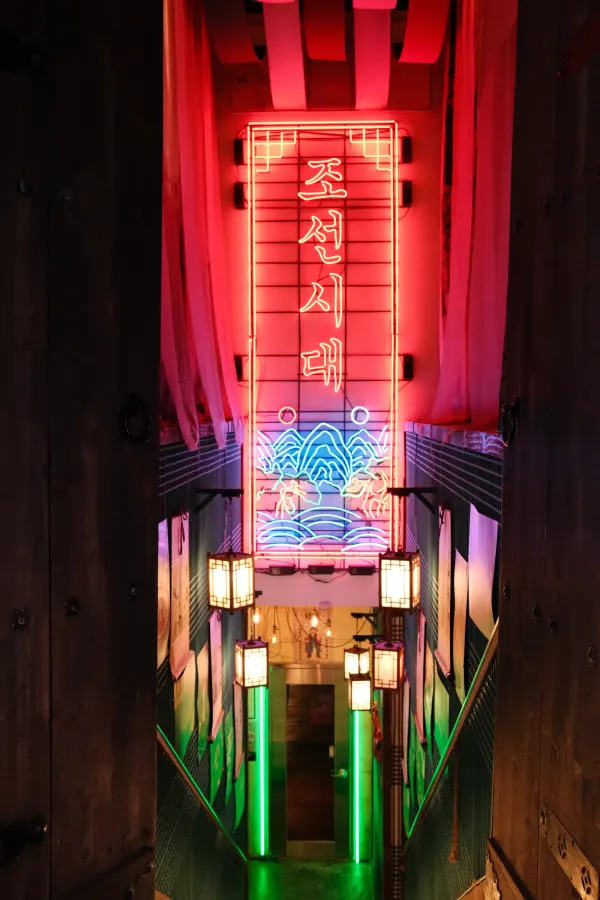 A narrow stairwell illuminated by red, blue and green neon signs
