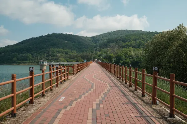 A brick walkway and wooden railings leading across water towards green hills