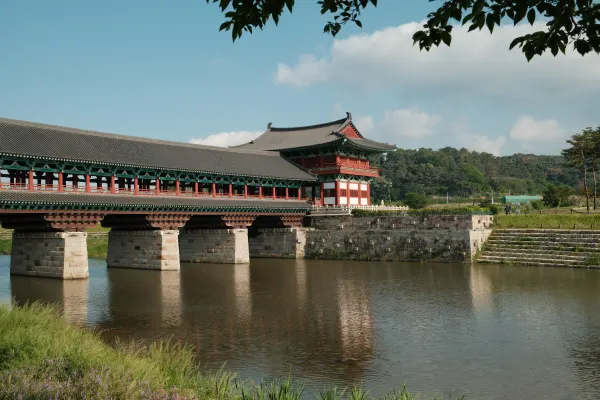 A red and green covered bridge reflected in a river beneath wooded hills