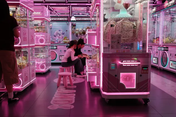 Two people playing claw machines in a pink neon arcade