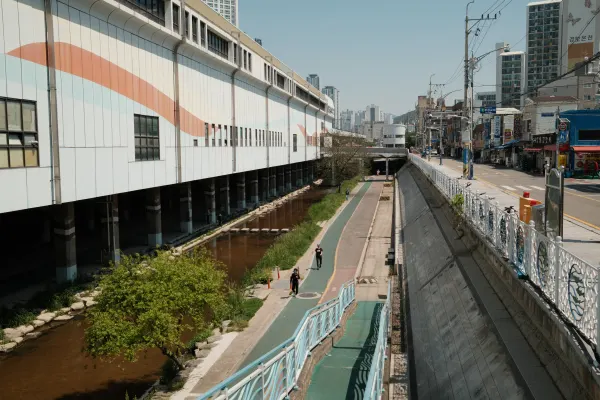 A streamside path running between a striped industrial building and a city road