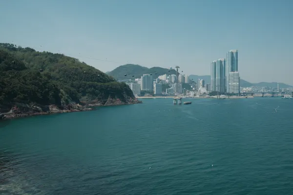 Turquoise water curving around a wooded headland towards waterfront towers
