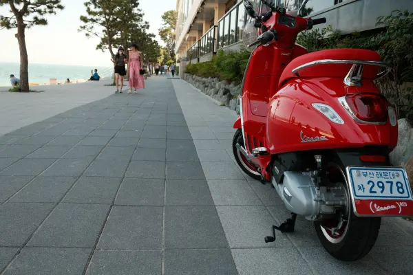 A red scooter parked beside a seaside promenade
