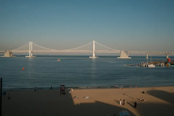 A white suspension bridge stretching across blue water above a beach
