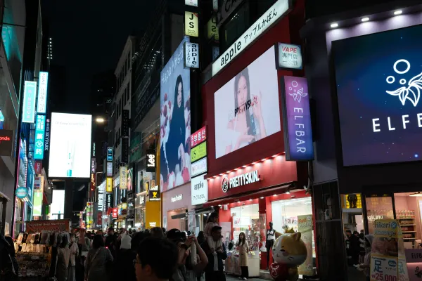 Crowds beneath large illuminated billboards and shop signs on a night street