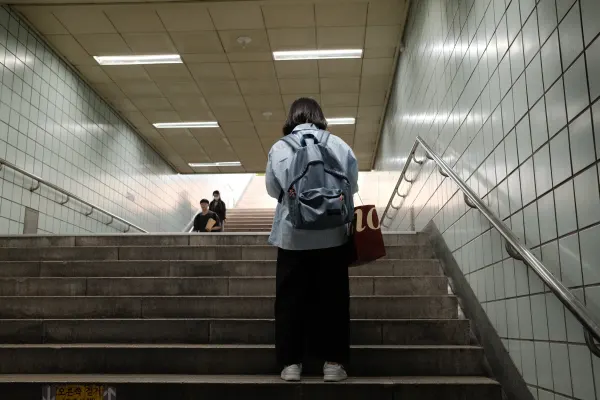 A person with a backpack climbing the stairs of a tiled underground passage