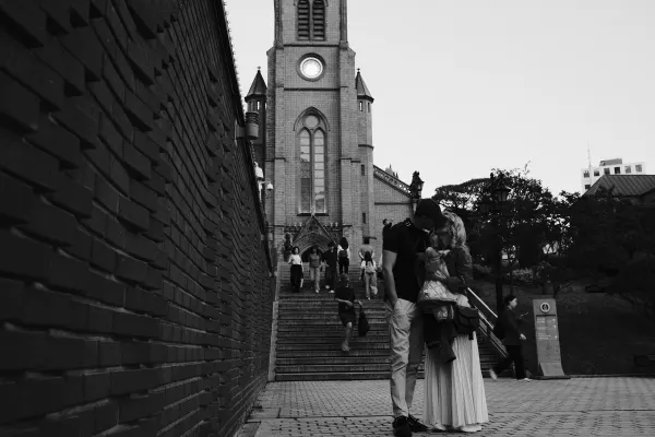 A couple kissing beside a brick wall and church steps, photographed in black and white