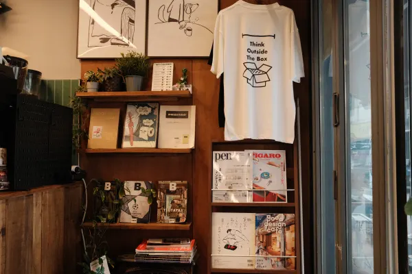 Books, magazines and a white T-shirt displayed on wooden shelves inside a cafe