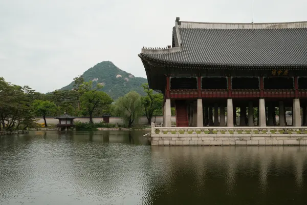 A traditional pavilion reflected in a pond with a mountain rising behind it
