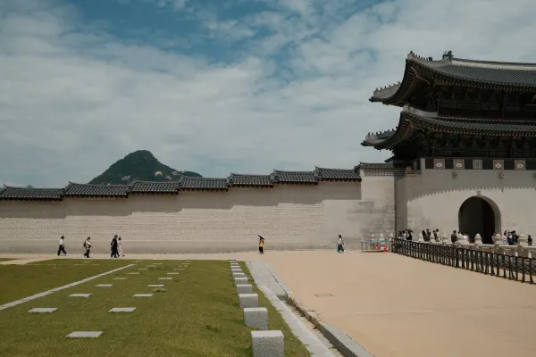 Small figures crossing an open palace courtyard beneath a broad white wall