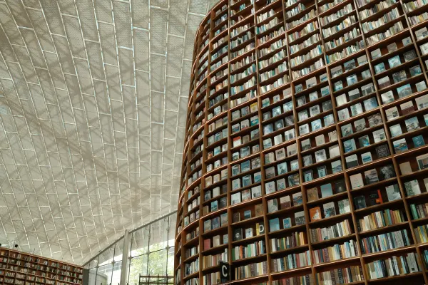 A towering curved bookshelf beneath the geometric glass roof of a library