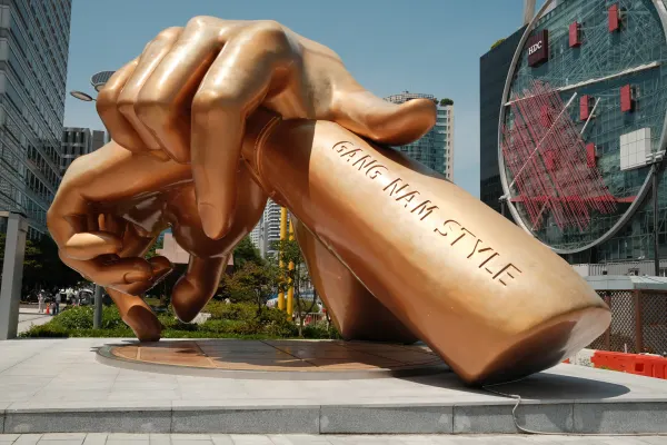A golden sculpture of crossed hands beneath tall city buildings