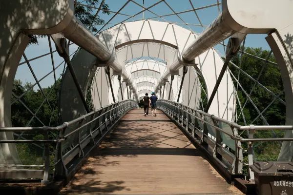 People crossing a covered footbridge beneath repeating white steel arches
