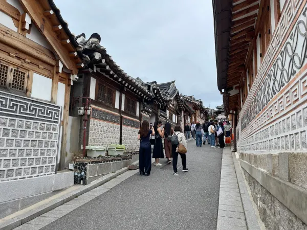 People walking between traditional tiled roofs and patterned walls in Seoul