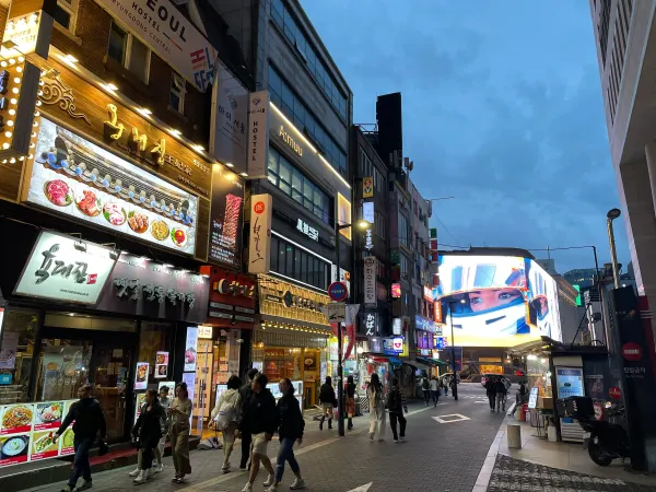 People walking past bright signs at dusk in Seoul