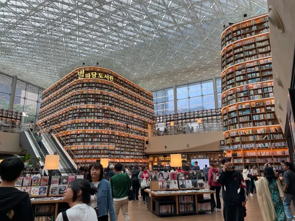 People beneath towering illuminated bookshelves and a patterned glass roof
