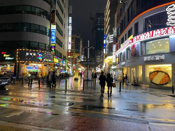 People and umbrellas crossing a brightly lit rainy street