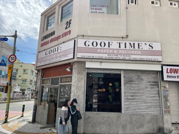 People outside a pale corner building marked Goof Times