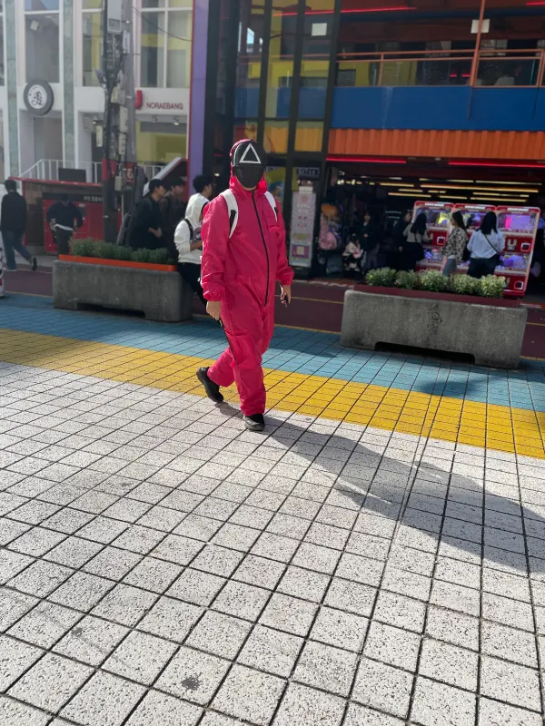 A person in bright pink crossing a sunlit city street