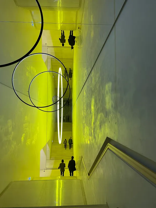 People reflected among luminous rings in a yellow staircase installation, Seoul