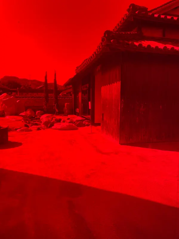 Traditional wooden buildings and a stone courtyard seen through saturated red glass