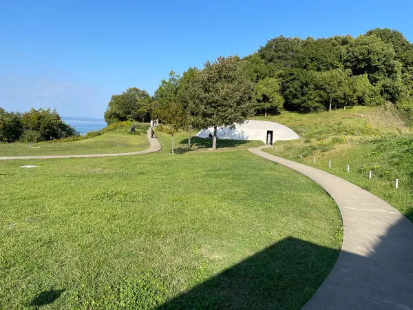A winding path and angular shadow leading towards a low white museum in a grassy hillside