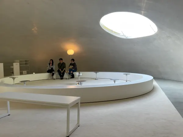 Visitors sitting beneath a round opening in a white concrete room
