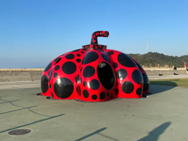 A red pumpkin sculpture covered in black dots beside the sea