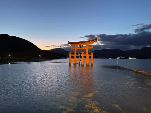 An illuminated shrine gate reflected in calm water at dusk