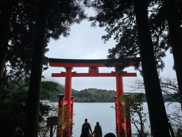 Silhouetted visitors beneath a red lakeside shrine gate