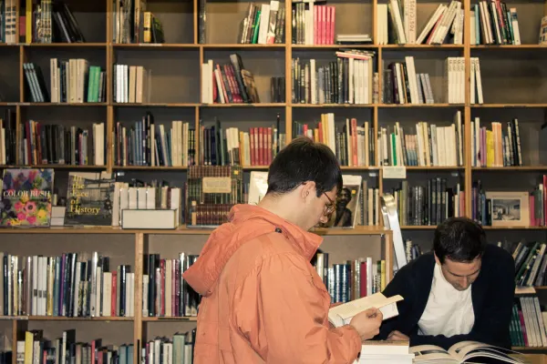 Two people reading books in front of tall bookshop shelves