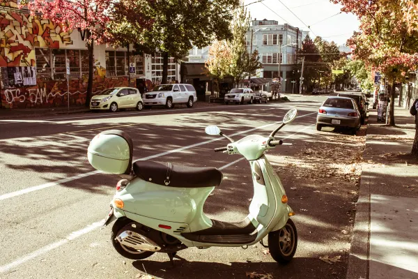 A pale green scooter parked beneath autumn trees