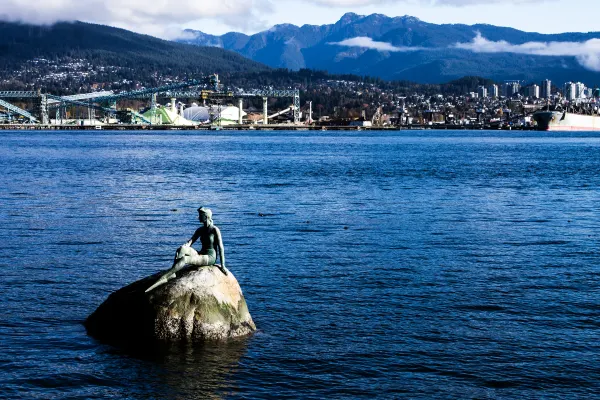 A figure sculpture on a rock with mountains across the harbour