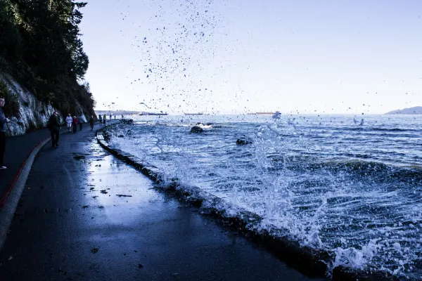 A wave splashing over the seawall beside walkers