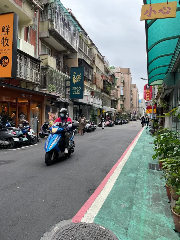 A rider on a blue scooter approaching along a street beside a turquoise footpath